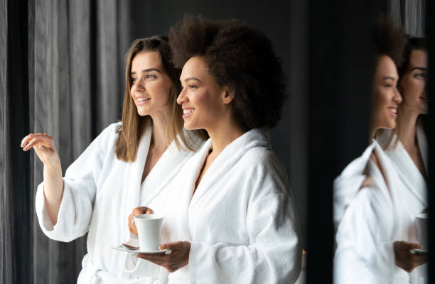 mujeres relajadas y bebiendo té en batas durante el fin de semana de bienestar - bathrobe women cup towel fotografías e imágenes de stock