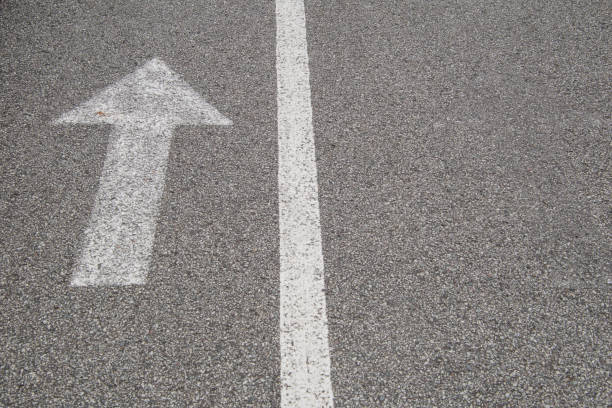 istock Arrow with a line, white paint on small grain asphalt. 1262641349