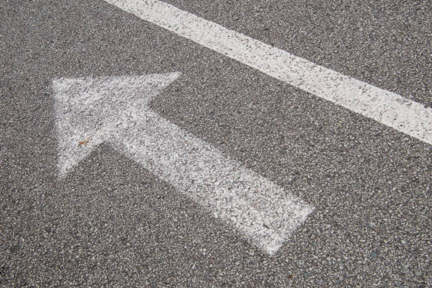 istock Arrow with a line, white paint on small grain asphalt. 1262641371