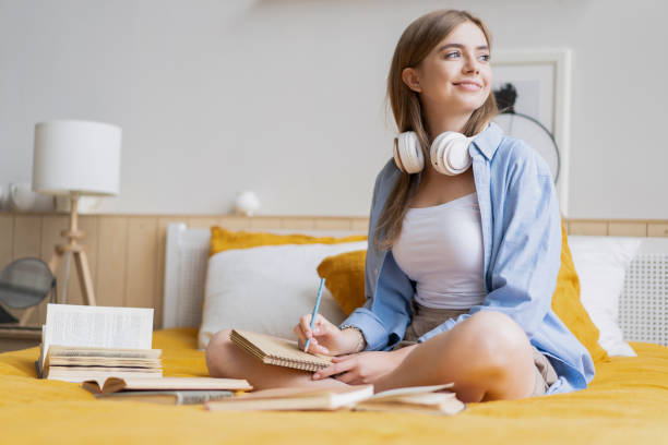 istock Attractive student woman laying on her bed at home while writing and working on her homework from college 1262651642
