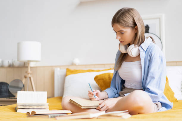 istock Attractive student woman laying on her bed at home while writing and working on her homework from college 1262651651