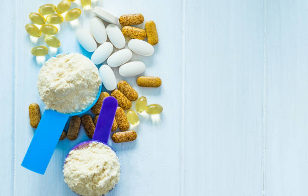 Closeup sport food supplements Closeup blue and purple measure dishes with protein powder and white-yellow sport pills around on the white table bodybuilding supplement stock pictures, royalty-free photos & images
