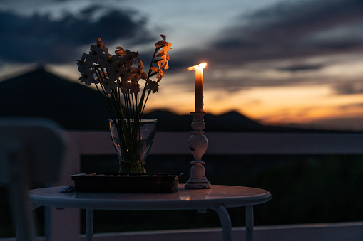 Minimalistic table setting for holiday romantic dinner, wooden table with flower and white candele. Selective focus. Beautiful mountains after sunset on the background