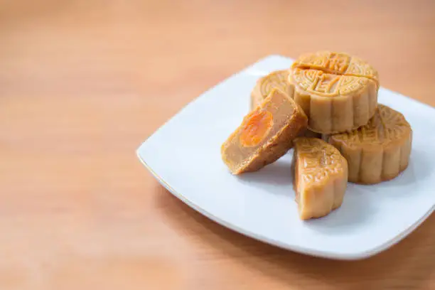 Photo of moon cakes in a Chinese mid-autumn festival cut in a half to see soy bean and egg yolk stuff inside on white plate