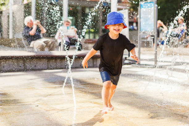 istock Little boy running between water jets in fountain 1262660422