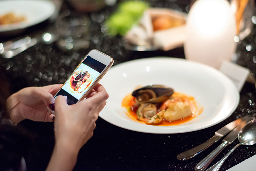girl Using Smart phone taking her italian seafood dish