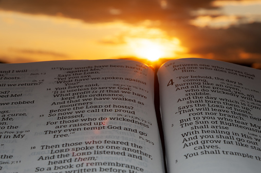 Holy Bible open at sunset with highlight on Malachi 4: 2. Background with clouds and sunbeams.