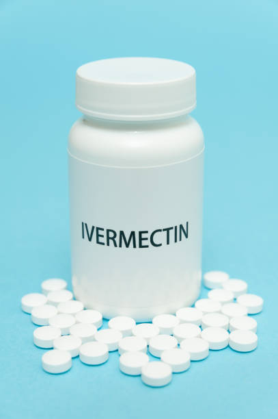 istock Treatments for Coronavirus (COVID-19): IVERMECTIN in white bottle packaging with scattered pills. Isolated on blue background. Vertical shot. 1262666484