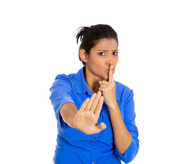istock serious woman placing finger on lips, pointing at you quiet, silence 1262670496