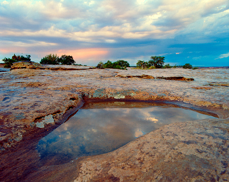 Beautiful pastel colors in the sky at sunset reflecting in a pool of water on the rocky plateau on top of a mesa at Canyon de Chelly