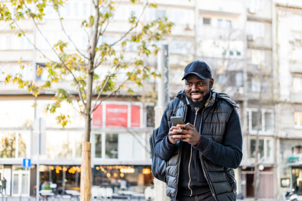 istock Cheerful African American man  using mobile phone application for searching cafes near location in downtown, happy dark skinned hipster guy read news from social network walking in city 1262683975