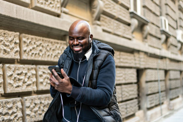 istock Cheerful African American man  using mobile phone application for searching cafes near location in downtown, happy dark skinned hipster guy read news from social network walking in city 1262684395