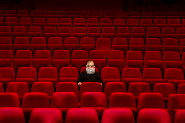 istock One man with white beard sits in Empty cinema or theatre with comfortable red seats 1262687002