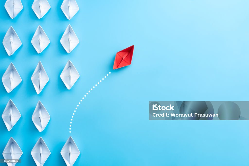 Group of white paper ship in one direction and one red paper ship pointing in different way on blue background. Business for innovative solution concept. Paper Boat Stock Photo