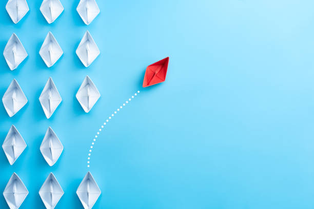 Group of white paper ship in one direction and one red paper ship pointing in different way on blue background. Business for innovative solution concept. stock photo