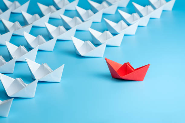 istock Leadership concept. Red leader paper ship leading among white on blue background. 1262688953