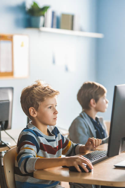 小学校コンピュータサイエンス教室:スマートリトルスクールの男の子は、ソフトウェアコーディングのためのプログラミング言語を学習し、パーソナルコンピュータ上で動作します。現代教 - elementary student little boys classroom child ストックフォトと画像