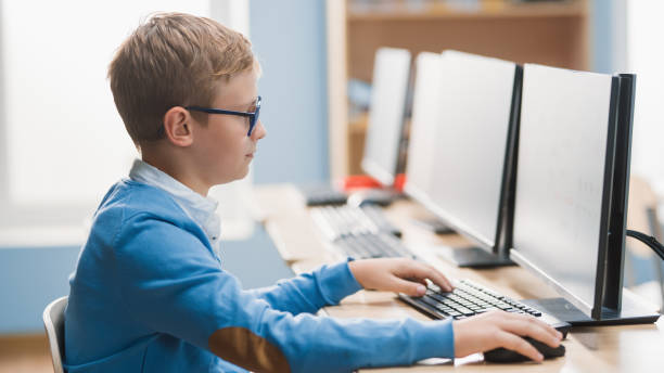 istock Elementary School Computer Science Classroom: Cute Little Boy wearing Glasses Uses Personal Computer, Learning Programming Language for Software Coding. 1262689306