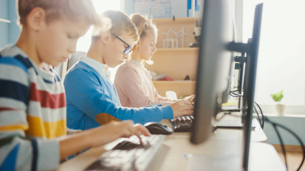 istock Elementary School Classroom: Portrait of a Smart Boy with Glasses Uses Personal Computer, Learning How to Use Internet Safely, Programming Language for Software Coding. Modern Education for Kids 1262689336