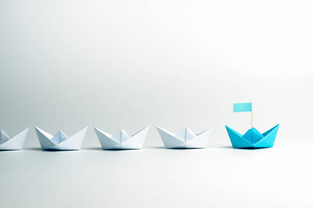 istock Leadership concept. Blue leader paper ship leading among white on white background. 1262689382