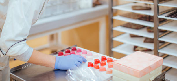 istock Confectioner in gloves putting tray with ruby truffles on shelf 1262690651