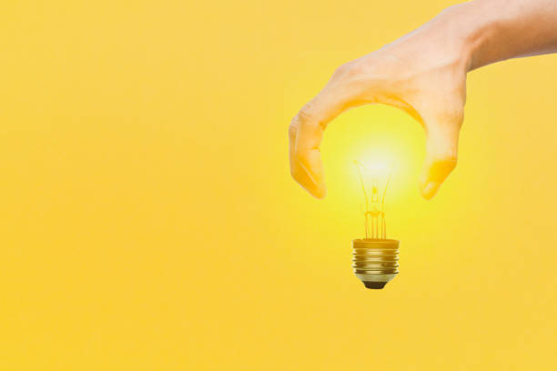 istock Light bulb by hand glowing on yellow background. Creativity, inspiration ideas concept. 1262690653