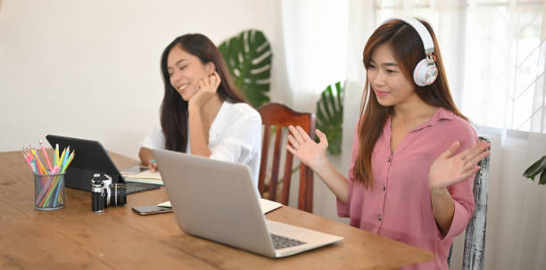 istock Women are using a computer tablet and laptop while sitting together at the wooden table. 1262694335