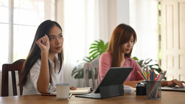 istock Women are using a computer tablet and laptop while sitting together at the wooden table. 1262694354