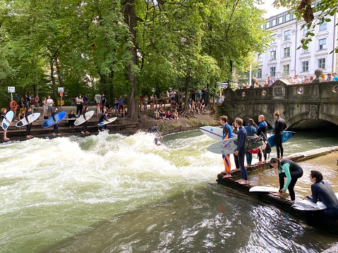 Munich, Germany - July, 21 - 2020: Surfer on the Eisbach river in Munich, Englischer Garten. Persons waiting in a row to jump in, surfing lasts from 3 seconds to 30 seconds.