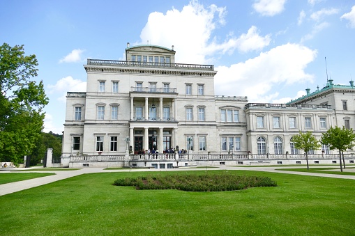 Essen, Germany - July, 29 - 2020: The Villa Hügel in the Bredeney district of Essen was built by Alfred Krupp in 1870–1873 and is the former residential and representative house of the Krupp industrial family. The castle-like villa has 8,100 square meters of living and usable space with 269 rooms and is located in a prominent location above the Ruhr Valley and Lake Baldeney in the 28-hectare hill park. Today, the Alfried Krupp von Bohlen and Halbach Foundation is the owner of the property. The Kulturstiftung Ruhr also has its headquarters in the villa. B. concerts or exhibitions. Numerous historical rooms as well as the historical exhibition Krupp can be visited during the regular opening times.
