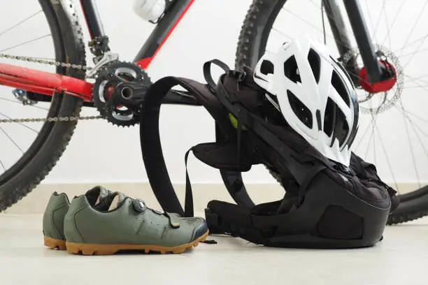 Mountain bike, velo shoes, backpack and white helmet at home.
