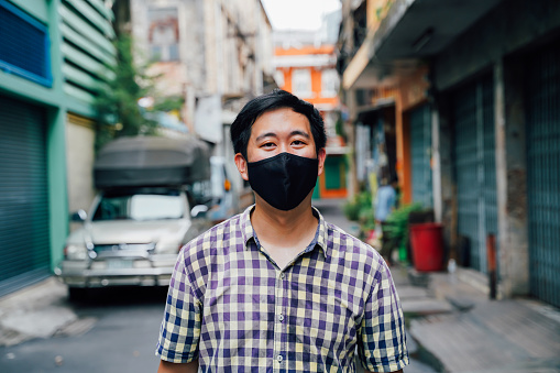 Portrait of one Asian man wearing a face mask on neighborhood street in Thailand, Southeast Asian city street style. Coronavirus - Covid19 new normal lifestyle.