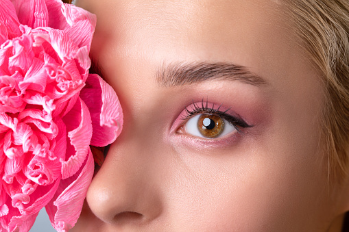 Portrait of a beautiful girl with blond hair, with beautiful creative pink makeup and healthy clean skin. There is a beautiful flower near her face. Makeup and cosmetology concept.