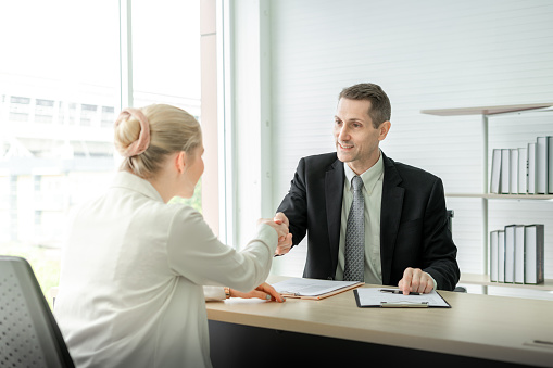 happy business man and woman shaking hands on desk in meeting room at office