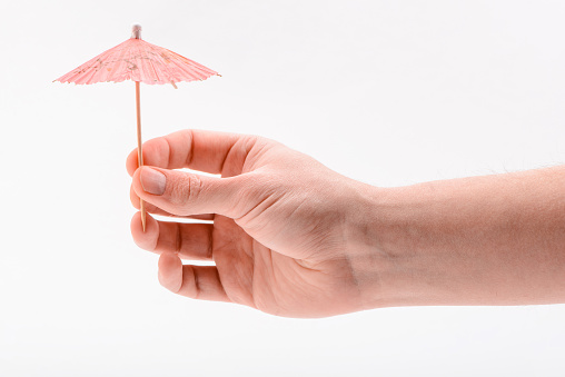 Hand holding a paper umbrella, isolated on white. Garnish for cocktails, dessert and other food and beverages.