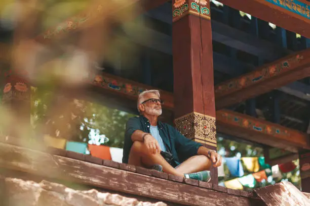 Photo of Senior man with beard rest in buddhist monastery. Elderly hiker has active journey. Exotic resort for pensioner