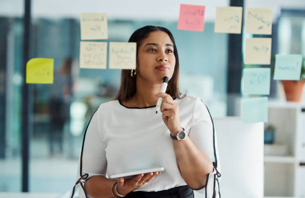 Thinking carefully about all her big ideas Shot of a young businesswoman using a digital tablet while brainstorming with notes on a glass wall in an office transparent wipe board stock pictures, royalty-free photos & images