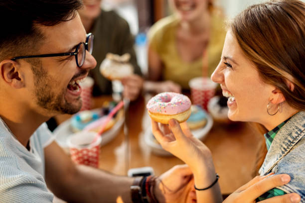 istock Cheerful couple having fun while eating donuts in a cafe. 1262749392