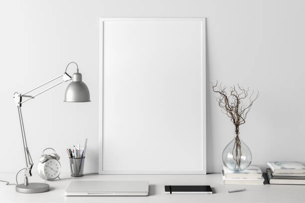 istock Vertical poster frame mockup on the white table of home studio workspace with white wall. Front view, clipping path around poster picture. 1262749396