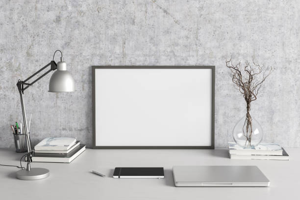 istock Horizontal poster frame mockup on the white table of home studio workspace with concrete wall. Front view, clipping path around poster picture. 1262749930