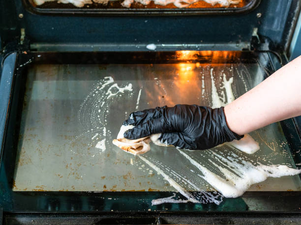 hand cleans glass door of dirty oven with reagent cleaning oven in home kitchen - female hand cleans glass door of dirty oven with reagent oven stock pictures, royalty-free photos & images