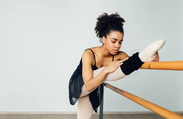 Female ballet dancer stretching her leg. Young woman preparing for a ballet class in a studio.