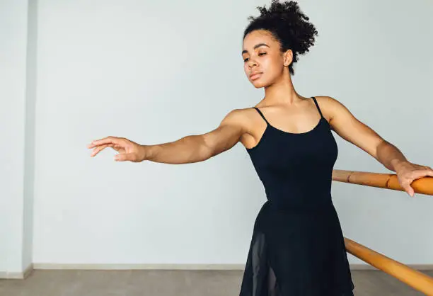 Young African American woman practicing ballet exercises holding a wooden handrail