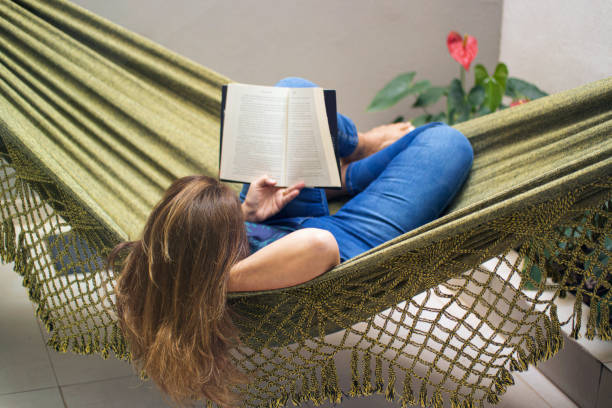 istock Woman reading a book at home, lying in a hammock. 1262757277