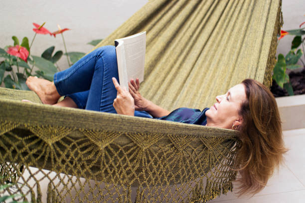 istock Woman reading a book at home, lying in a hammock. 1262757376