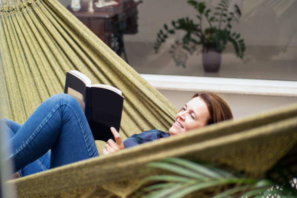 istock Woman reading a book at home, lying in a hammock. 1262757469