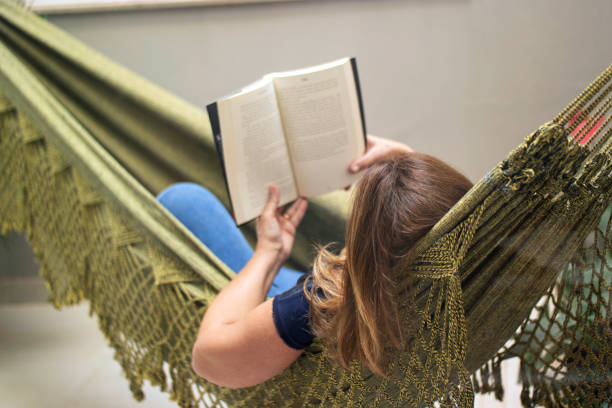 istock Woman reading a book at home, lying in a hammock. 1262757661