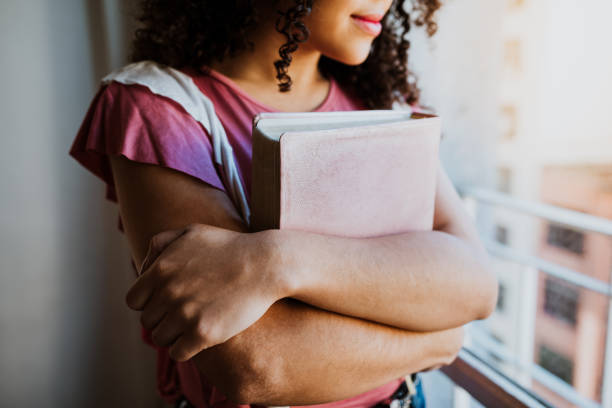 Unrecognizable woman embraced with bible in window light