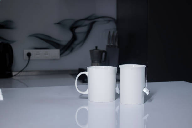 istock two white cups with tea and sticking out tea bags on a white table in a gray kitchen 1262761818