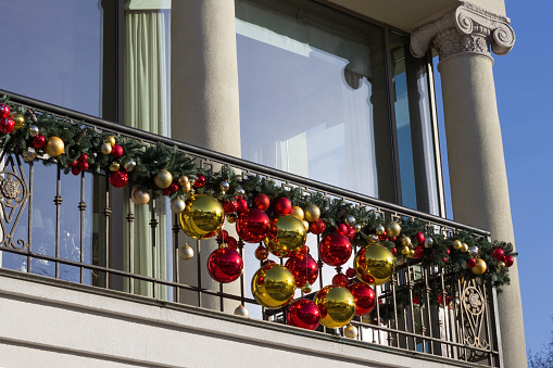 Balcony railings are decorated with tree branches and toys. Wide windows and columns on balcony